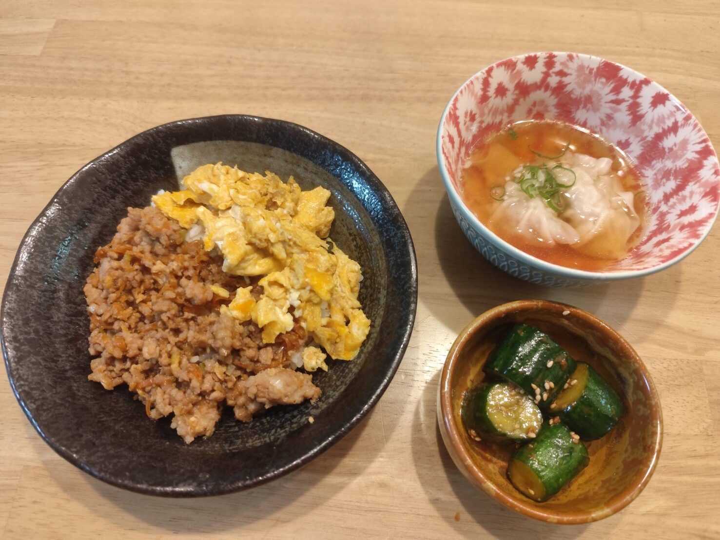 そぼろと炒り卵の二食丼、ワンタンスープ、きゅうりのごま和えが並ぶ家庭料理の夕食。
