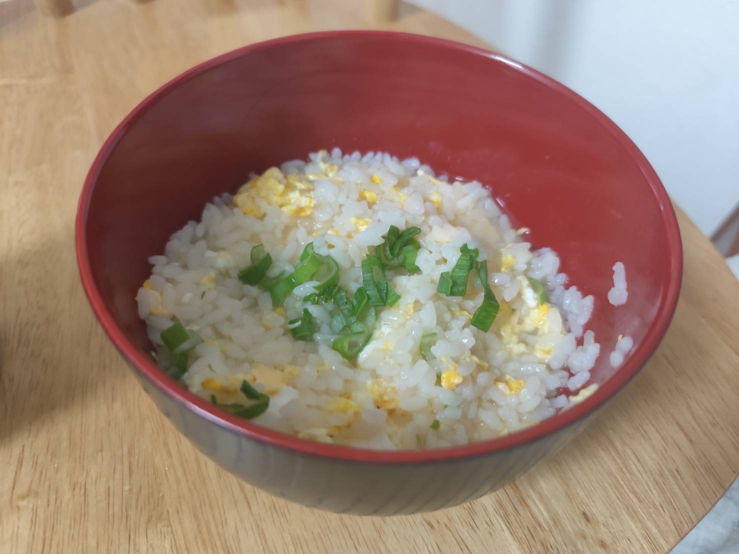 赤いお椀に盛られた卵入りのおじや。卵とご飯を煮込み、刻みネギを散らした旦那さんの優しい手料理。