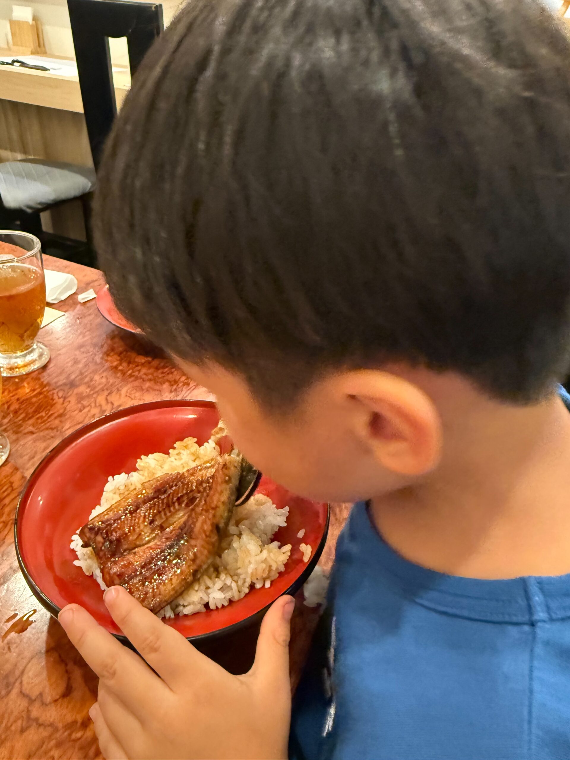 3歳の息子が大好物のうなぎごはんを夢中で食べている様子。赤い丼に白ご飯とタレの絡んだうなぎが盛り付けられている。

