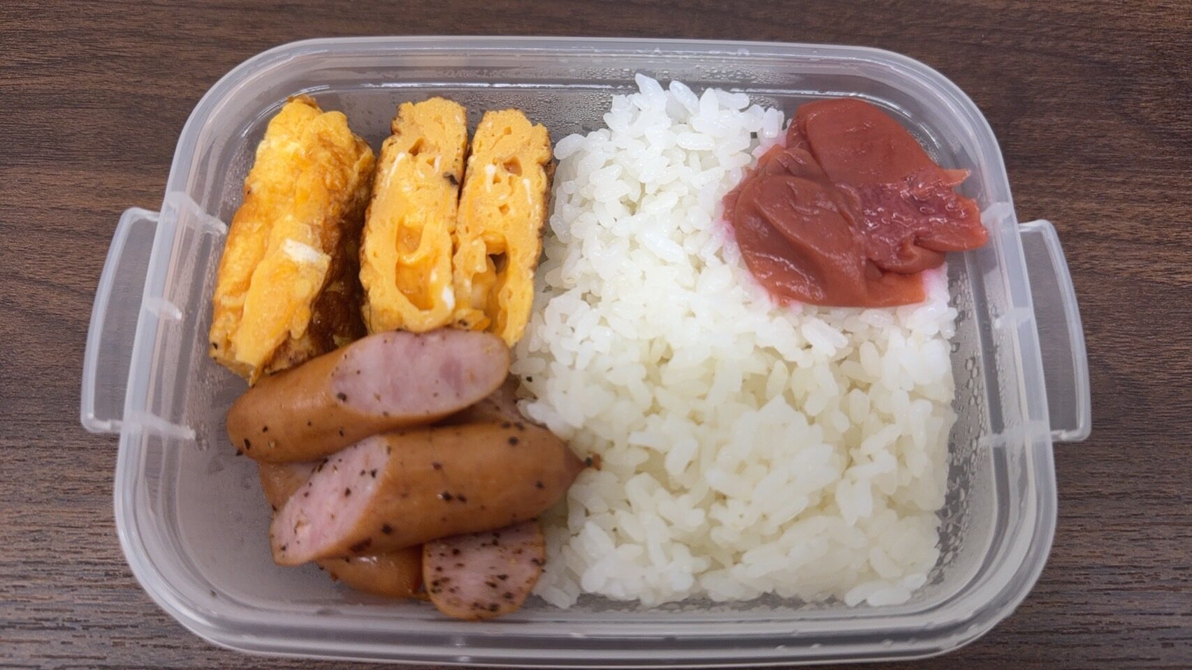 卵焼き・ウィンナー・梅干しご飯が入ったシンプルなお弁当の写真。