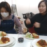 事務所で行われた試食会で、ミートソースパスタとサラダを前に談笑する2人の女性。