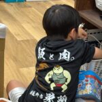 「飯と肉。」のオリジナルTシャツを着た子ども。背中には力強いキャラクターと店名ロゴが入っている。