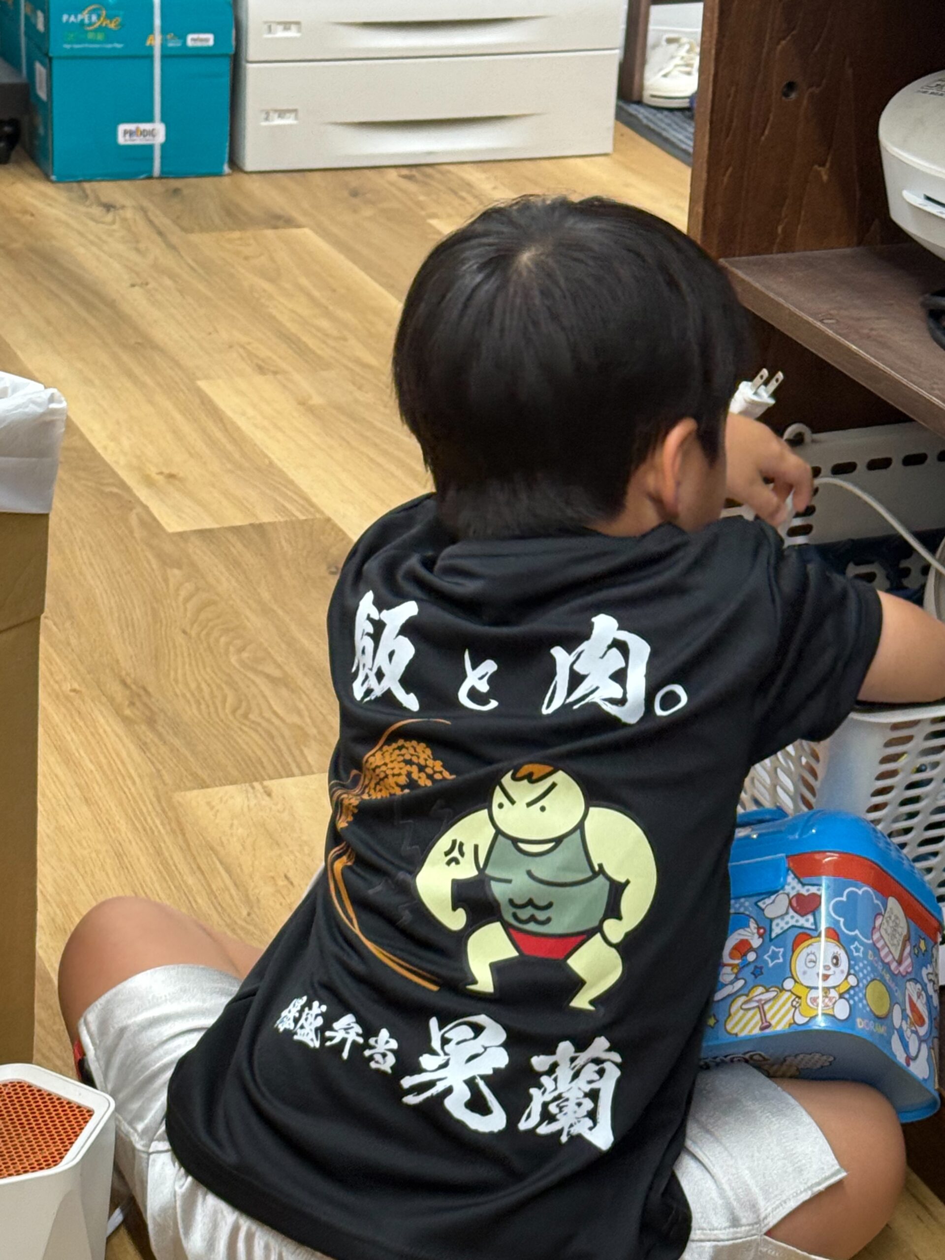 「飯と肉。」のオリジナルTシャツを着た子ども。背中には力強いキャラクターと店名ロゴが入っている。