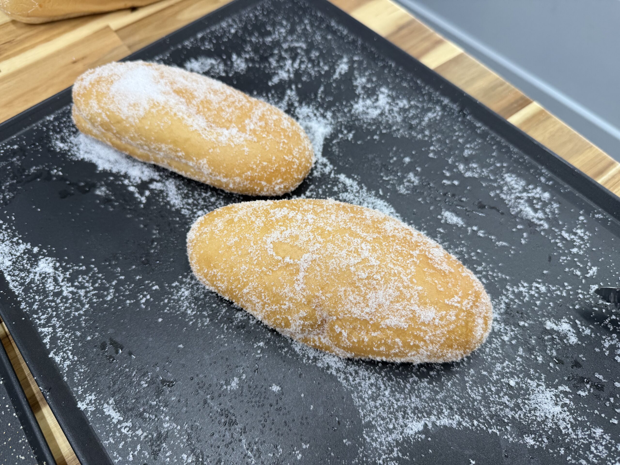 当店で焼き上げた自家製コッペパンをグラニュー糖で包み込んだ揚げパン。昔懐かしい給食の味を再現した人気商品。