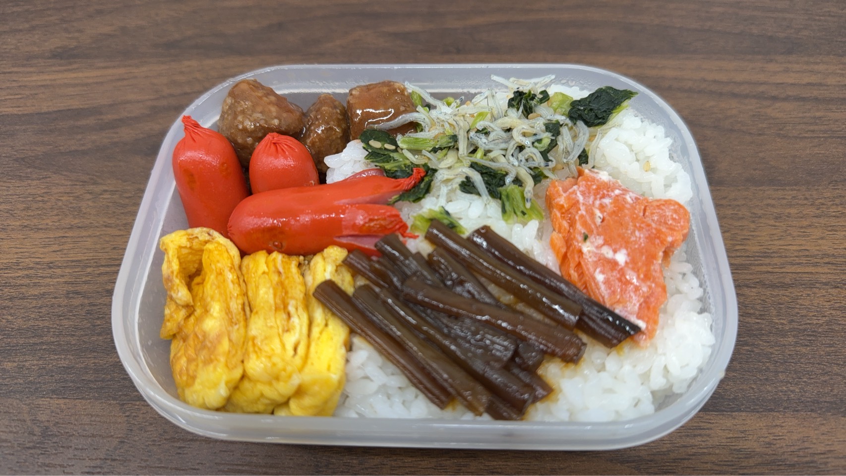 ウインナーや卵焼き、鮭、山菜の佃煮が彩りよく盛り付けられた手作り弁当の写真