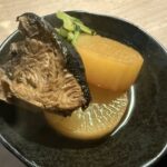 黒い器に盛り付けられたブリ大根と大根の煮物のアップ写真