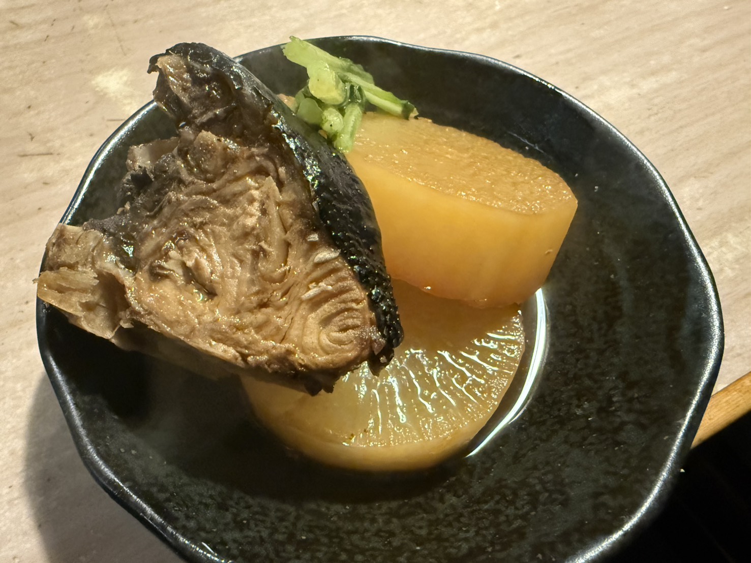 黒い器に盛り付けられたブリ大根と大根の煮物のアップ写真