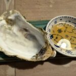 中身を食べ終えた大きな生牡蠣の殻と猫柄の小皿に入ったポン酢の写真