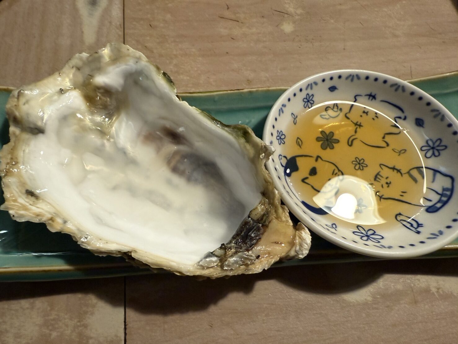 中身を食べ終えた大きな生牡蠣の殻と猫柄の小皿に入ったポン酢の写真