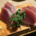 木の板に盛り付けられた分厚いハツガツオの刺身とパセリのアップ写真