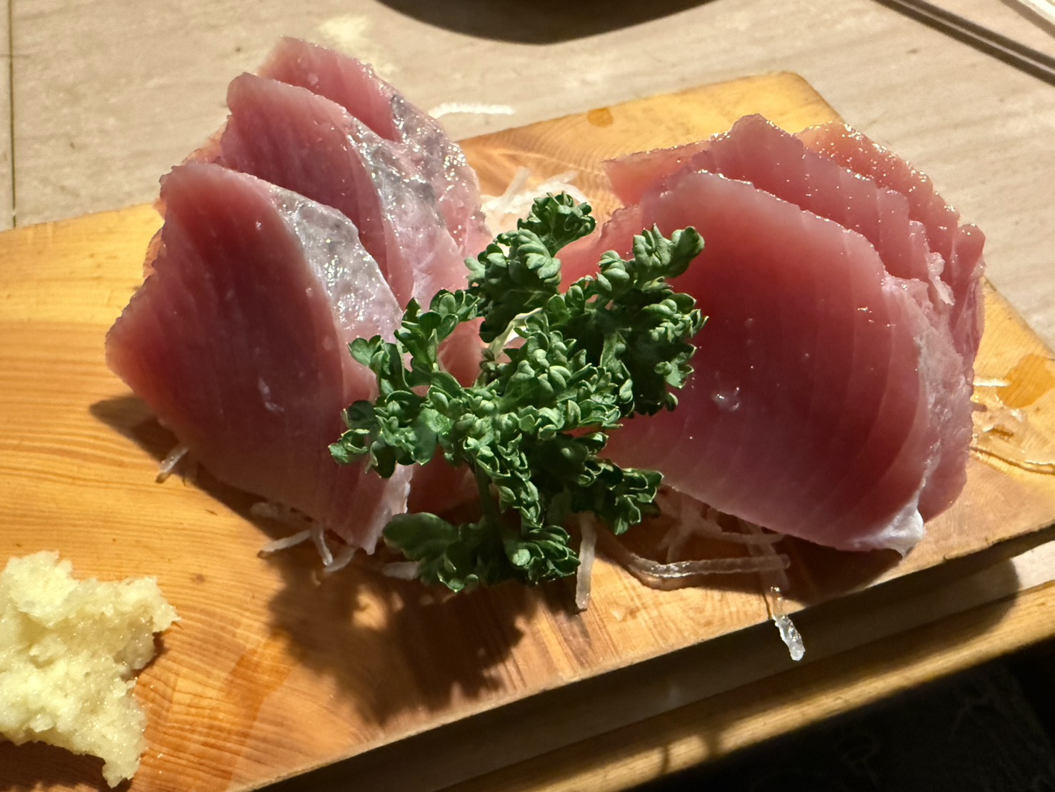 木の板に盛り付けられた分厚いハツガツオの刺身とパセリのアップ写真