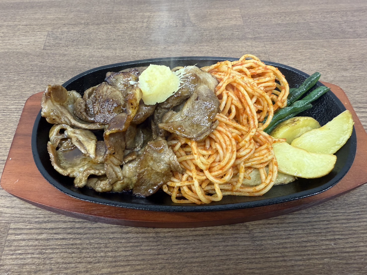 鉄板の上に盛り付けられた豚の生姜焼きとナポリタン、ポテトとインゲンのプレートの写真