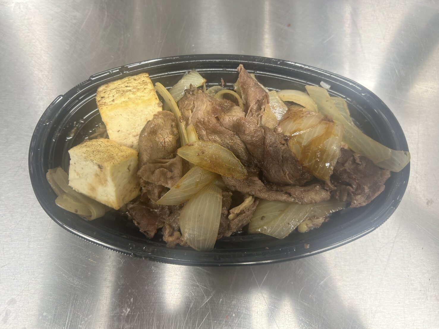 黒い容器に盛り付けられた牛肉と玉ねぎと焼き豆腐のすき焼き弁当のアップ写真