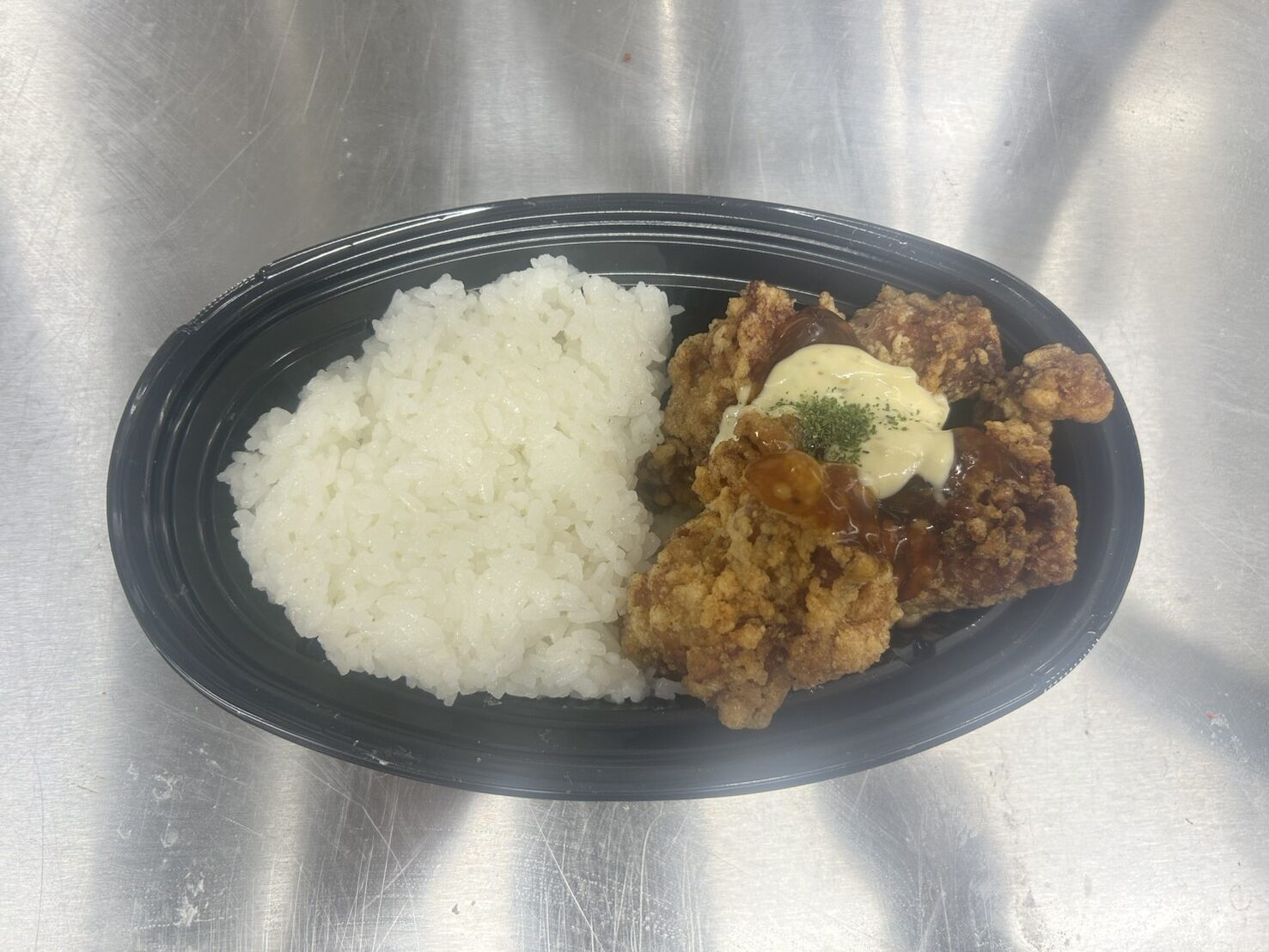 黒い楕円形の容器に白ご飯とタルタルソースがかかったチキン南蛮が盛られた弁当の写真