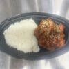 黒い楕円形の容器に白ご飯と白ごまがかかったヤンニョムチキンが盛られた弁当の写真