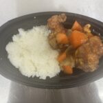 黒い楕円形の容器に白いご飯と酢鶏が半分ずつ盛られている弁当の写真