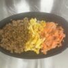 黒い容器に鶏そぼろ・炒り卵・鮭フレークが三色に並んだ三色丼の写真