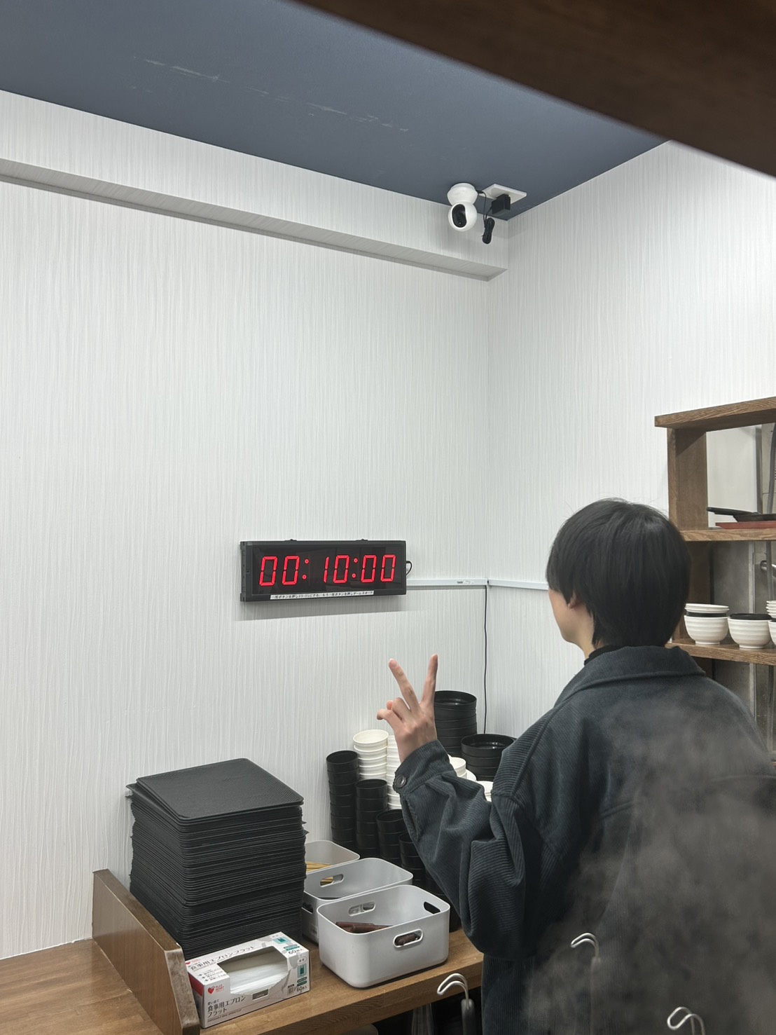 飯と肉。の店内でデジタルタイマーが00:10:00を表示し、1,000円ステーキ定食の10秒チャレンジ成功をピースサインで喜ぶお客様の後ろ姿の写真