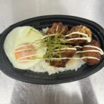 黒い楕円形の容器にご飯、その上に甘辛ダレとマヨネーズをかけた唐揚げと半熟目玉焼き、刻み海苔がのったマヨ唐丼の写真